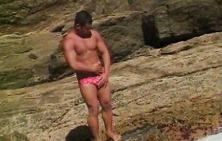 Hunk dude shows his tanned body on a rocky shore
